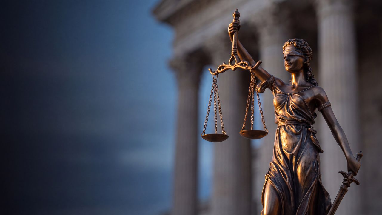 Bronze statue of Lady Justice holding scales in front of a courthouse
